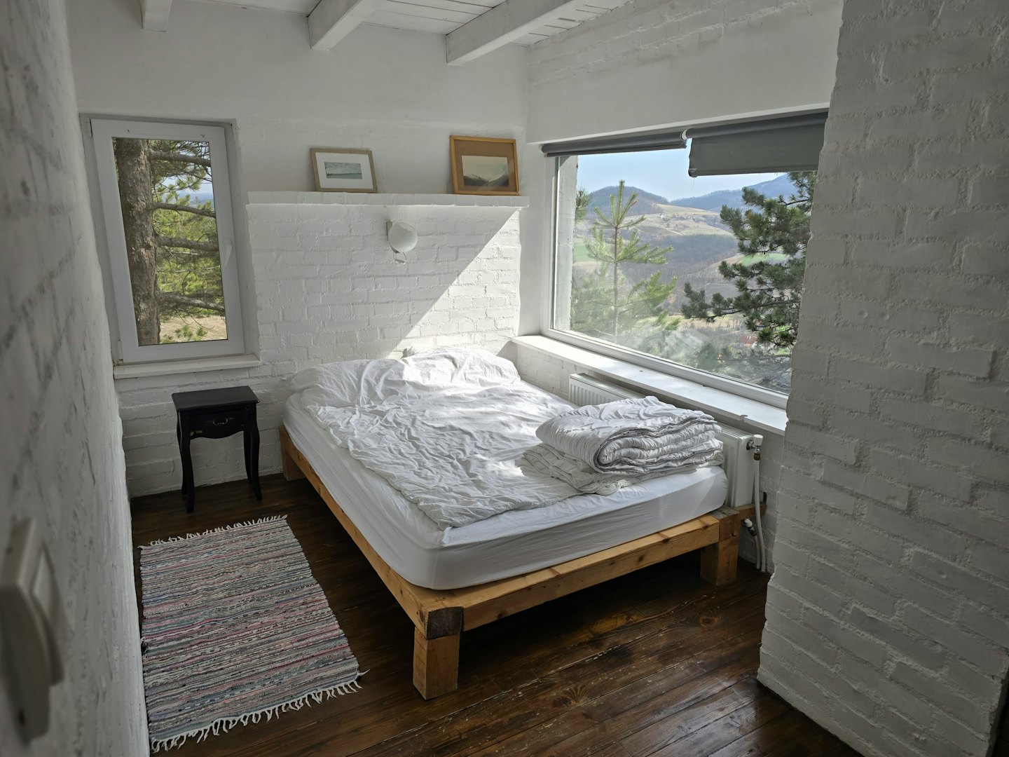 Camera da letto rustica con pareti in mattoni bianchi e vista sulle colline verdi.