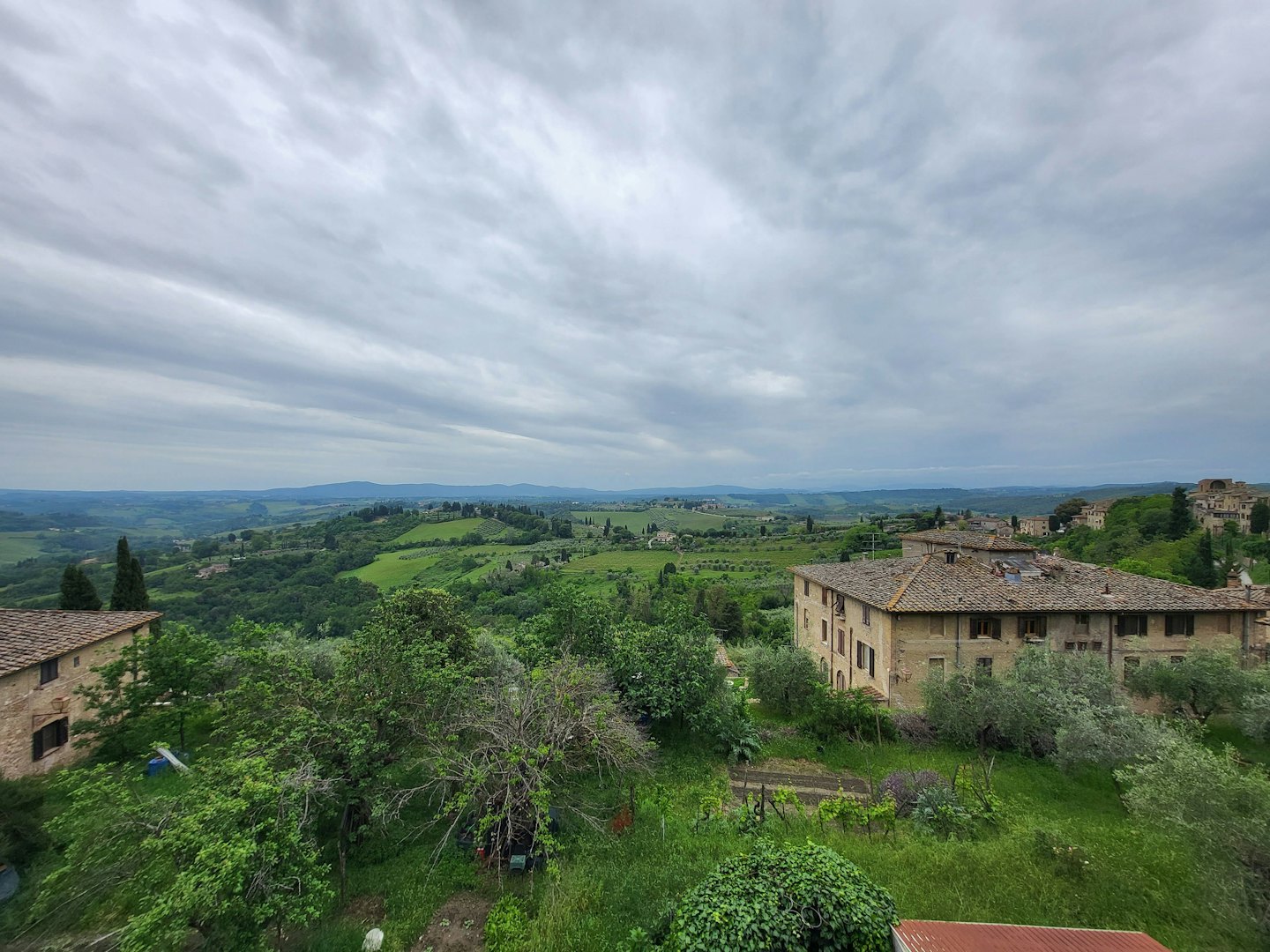 Colline verdi con vigneti e costruzioni in pietra sotto un cielo coperto.